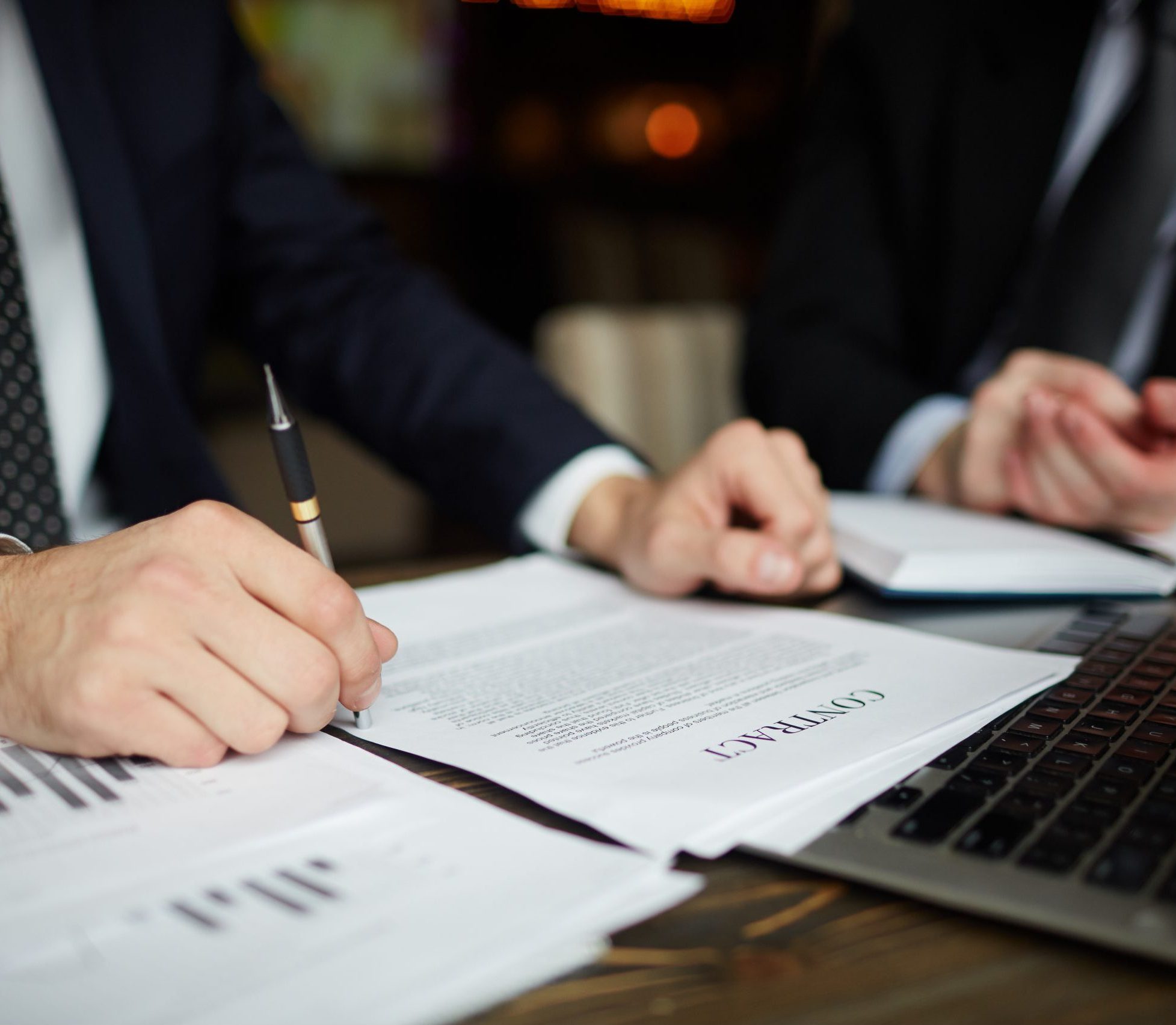 Closeup portrait of unrecognizable successful businessman wearing black formal suit reviewing documents and signing contract during meeting